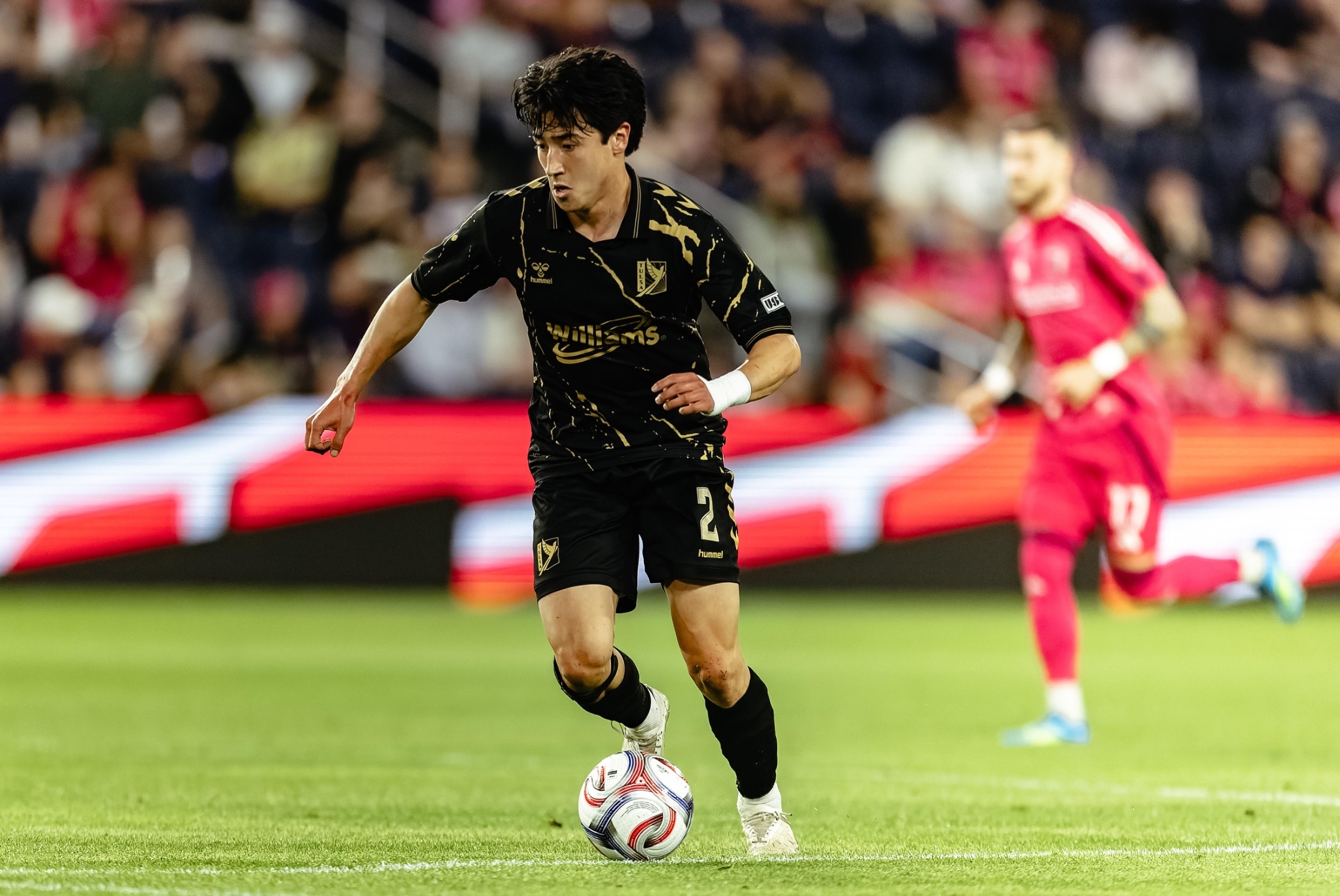 Owen Damm carrying the ball forward during a match with another recognizable player visible in the background