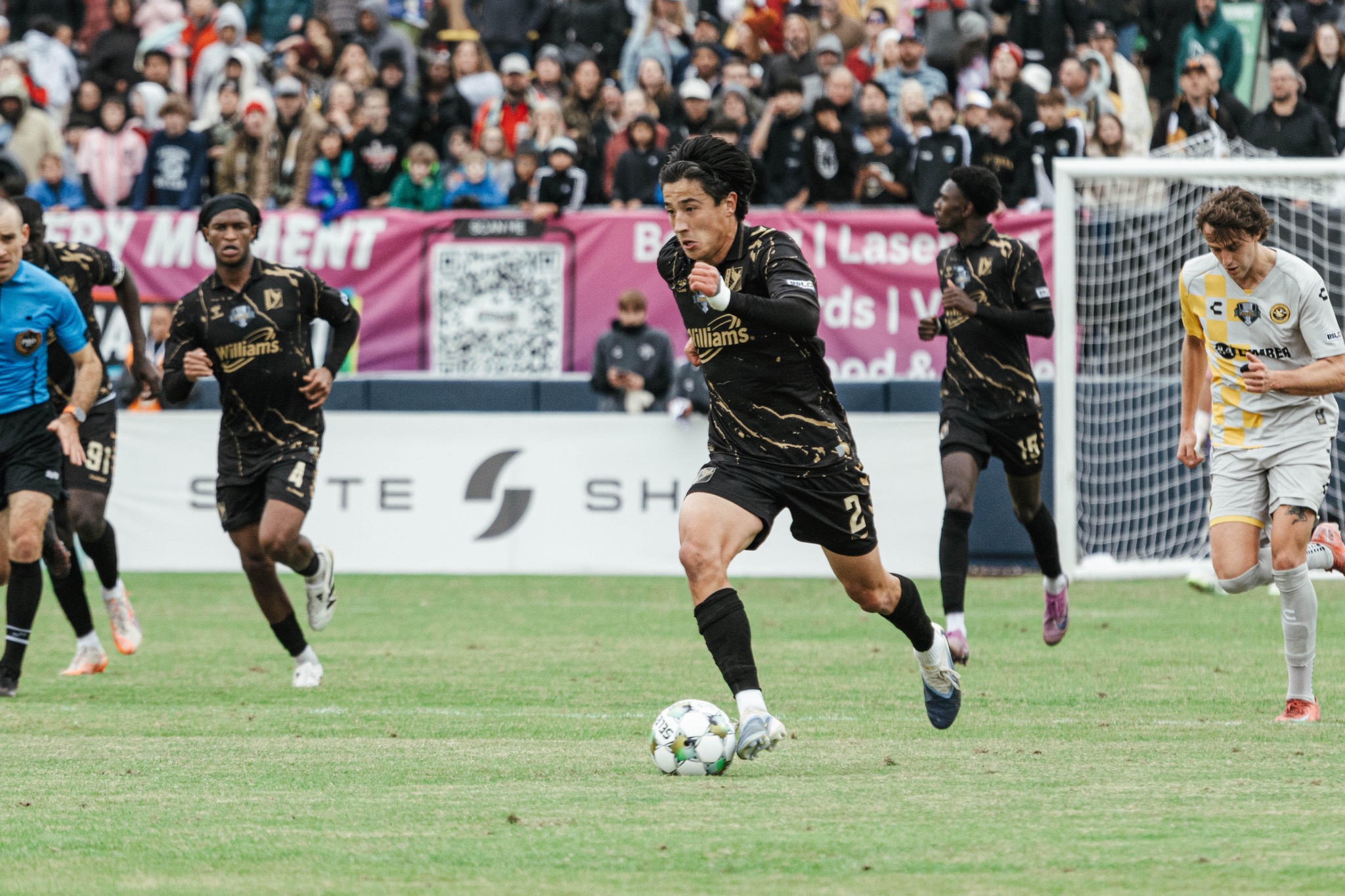 Owen Damm dribbling forward during a match with teammates and opponents in frame